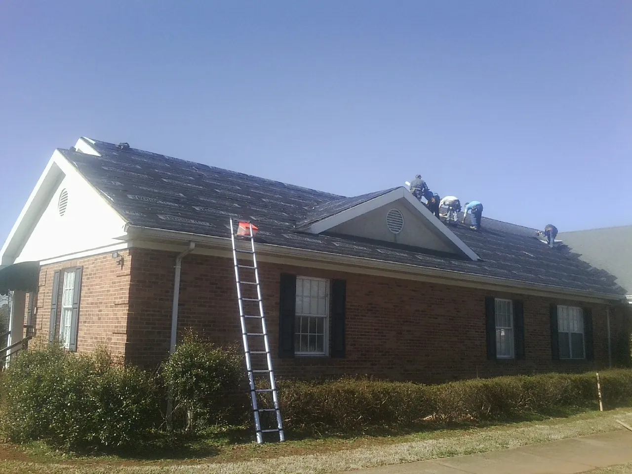 Crew tearing shingles off a brick ranch roof with a ladder set — Emergency Roof Repair work by our crew in Staffordsville