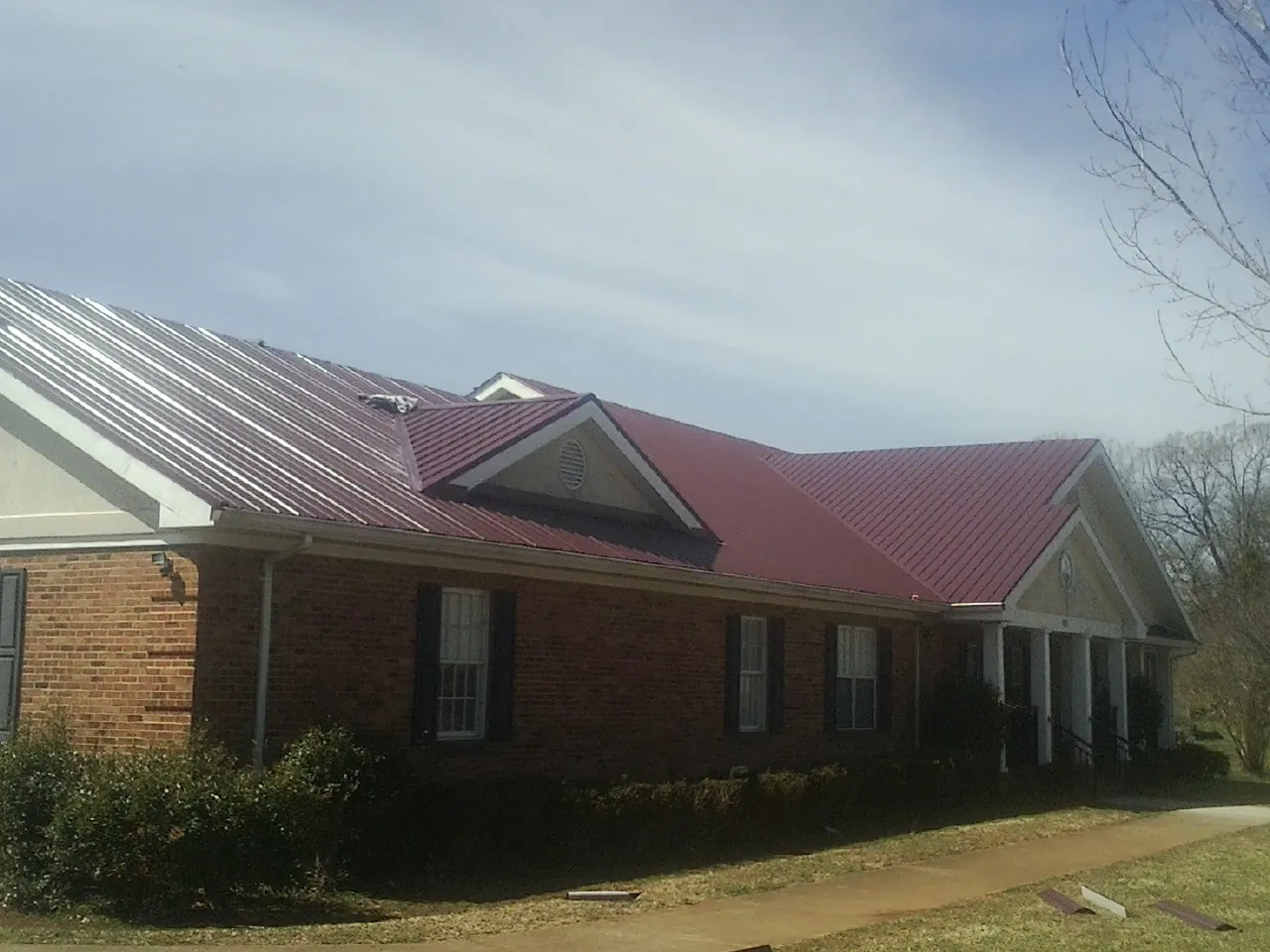 Red metal roof with gabled entries on a long brick building, from a Hail Damage Roof Repair job in Staffordsville