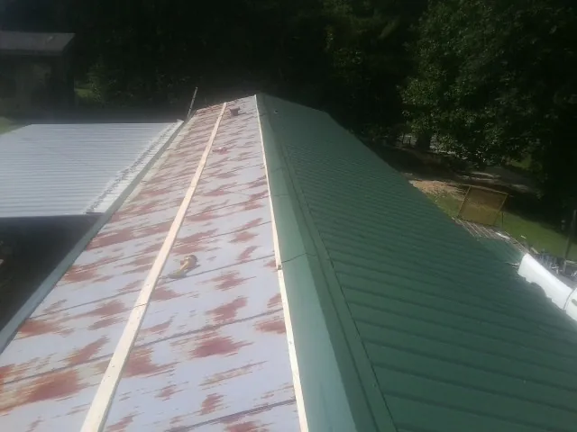 Old rusted panels beside newly installed green metal roofing — Wind Damage Roof Repair by Roofing Brothers in Staffordsville