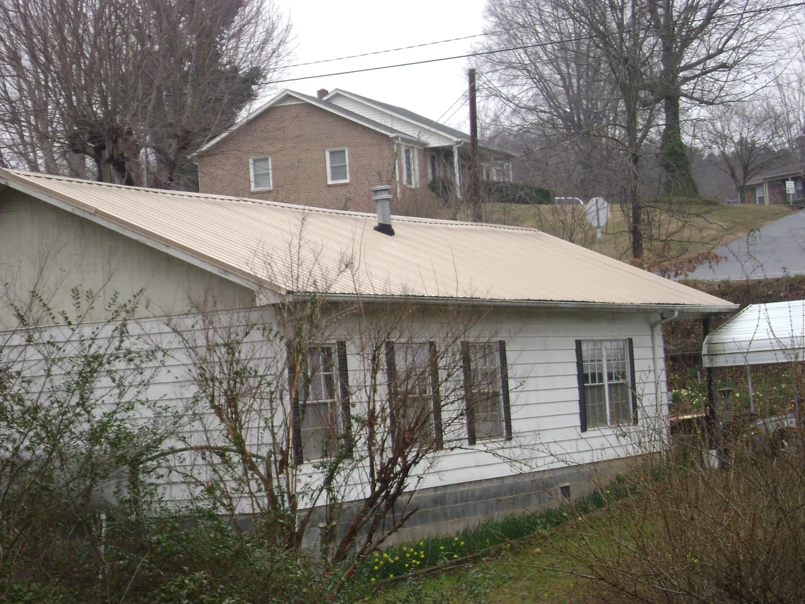 Tan metal roof on a white sided house set into a hillside — Commercial Roofing by Roofing Brothers in Staffordsville
